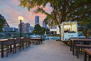 An outdoor seating area with tables and chairs, a pool, and a bar truck labeled 'BAT BAR' in the background. - Hyatt Regency Austin (Austin)