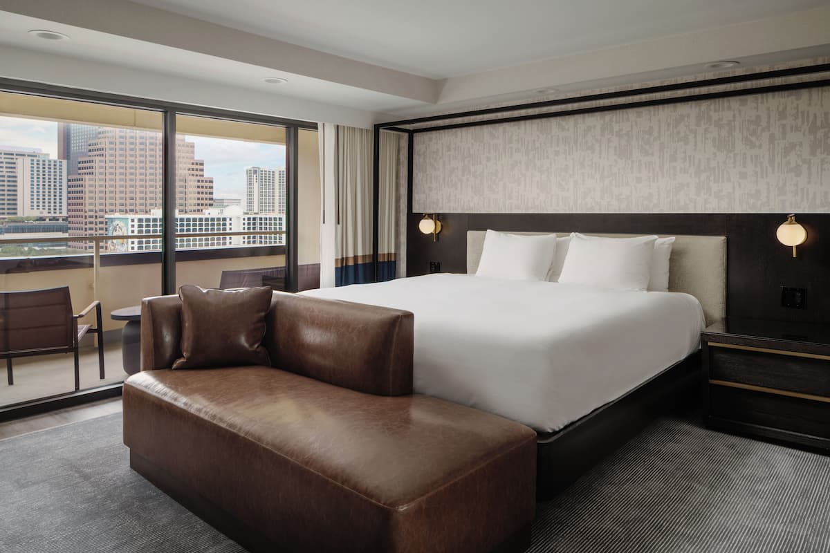 A hotel room with a large bed, a sofa, a desk, and a view of the city.