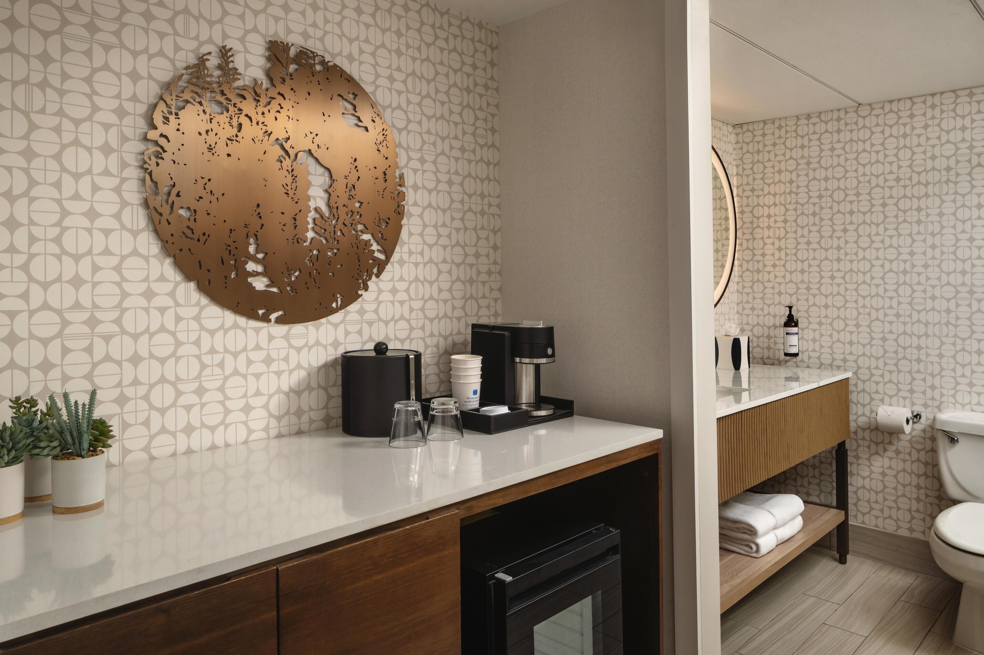 Une salle de bain moderne avec un mur orné d’un motif, un élément décoratif rond, une machine à café et des toilettes.