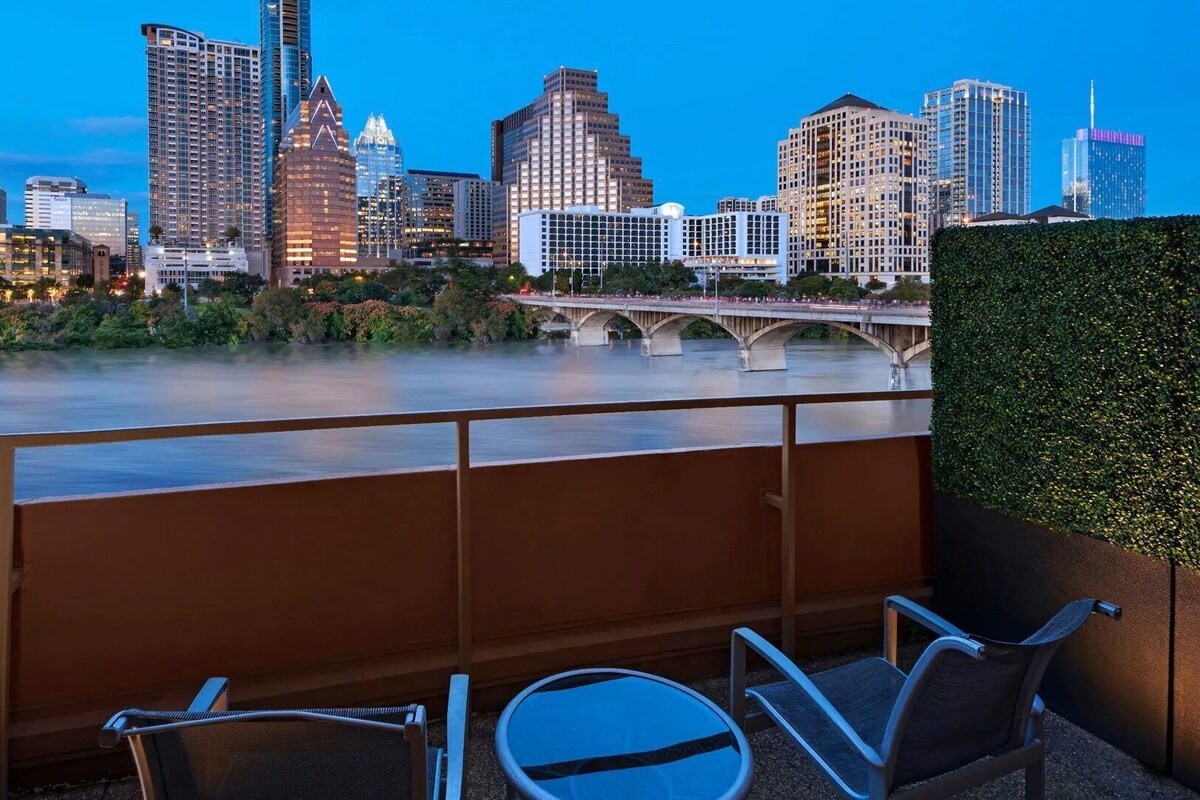 A balcony with chairs overlooking a city skyline and a river.