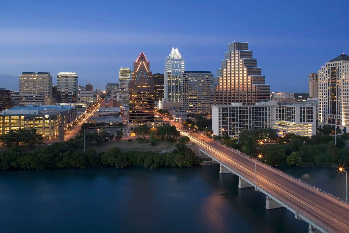 A city skyline with modern buildings, a river, and a bridge.