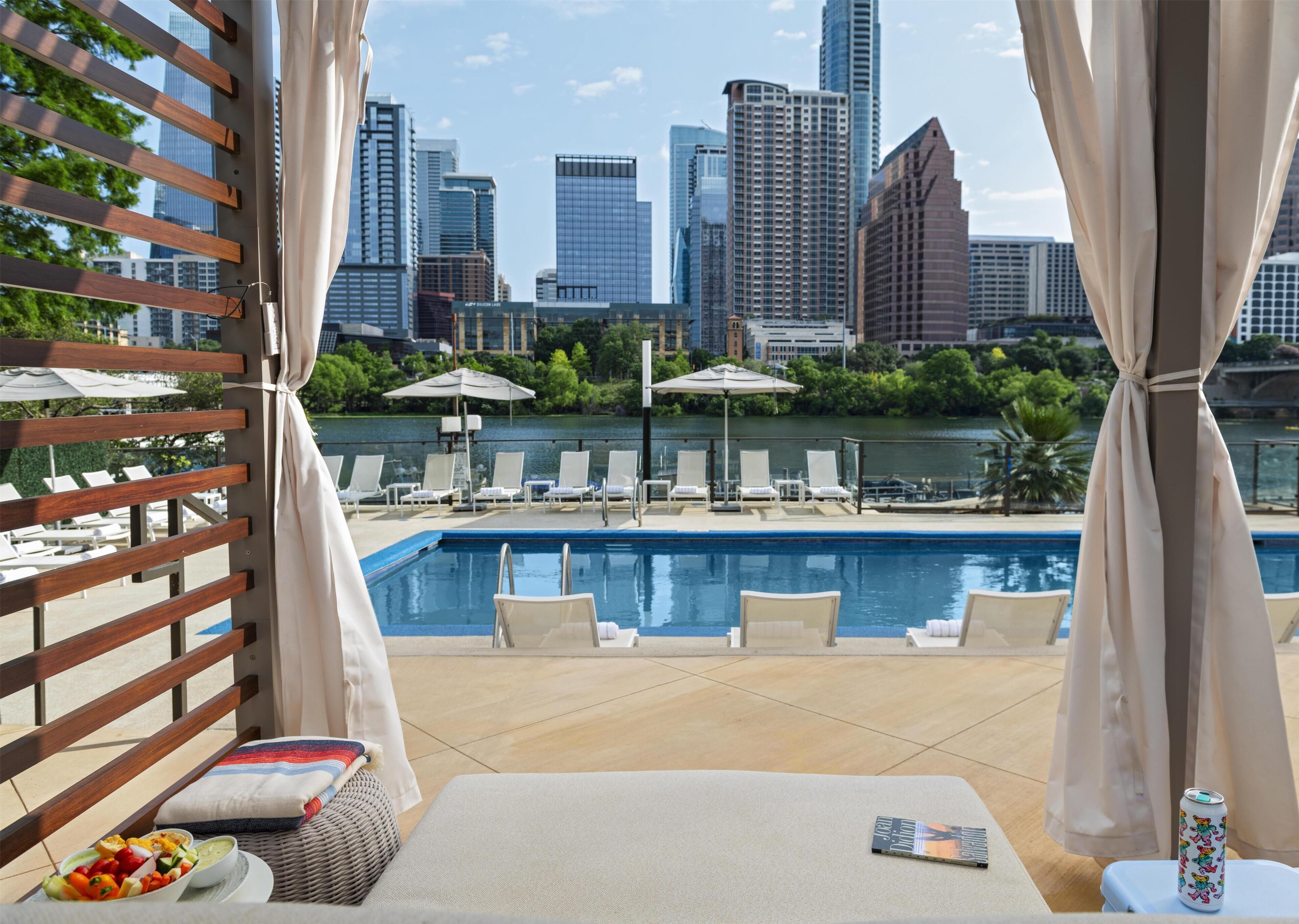 Un espace aménagé au bord de la piscine, avec des chaises longues, une table à manger où est servie une salade, et une vue sur les gratte-ciel de la ville.