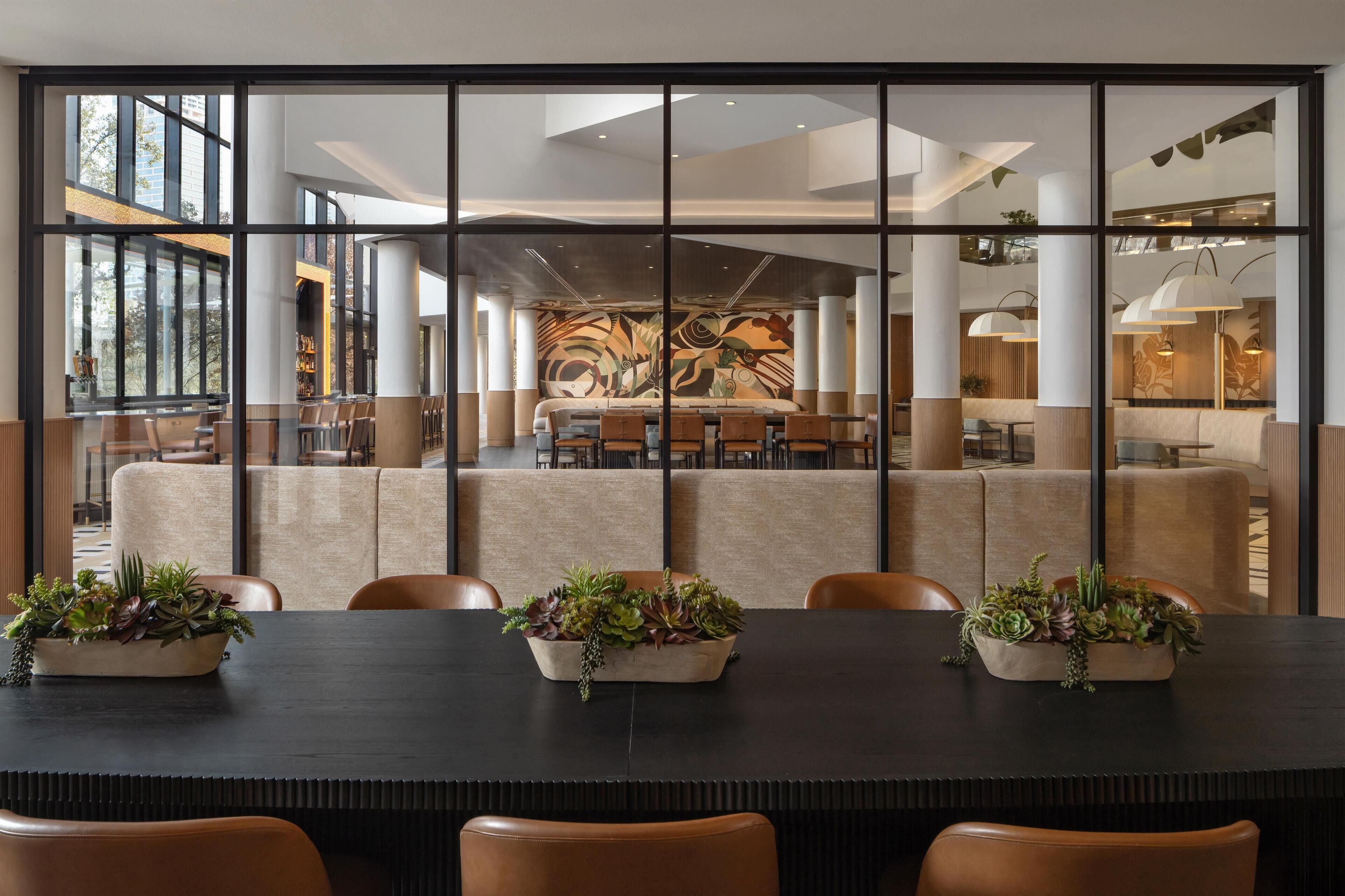 Un interior moderno con una gran mesa de comedor, sillas y plantas en macetas.