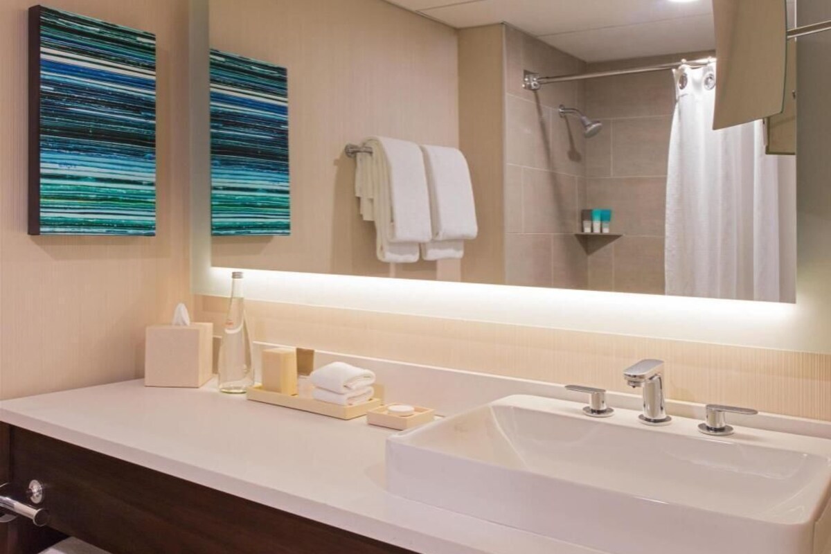 A modern bathroom with a large mirror, white sink, and two towels hanging on the wall.