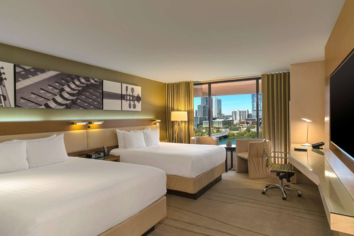 A hotel room with two beds, a desk, a chair, a TV, and a city view.