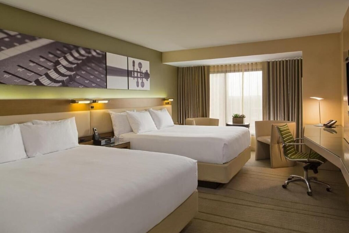 A hotel room with two beds, a desk, a chair, and a large window with curtains.