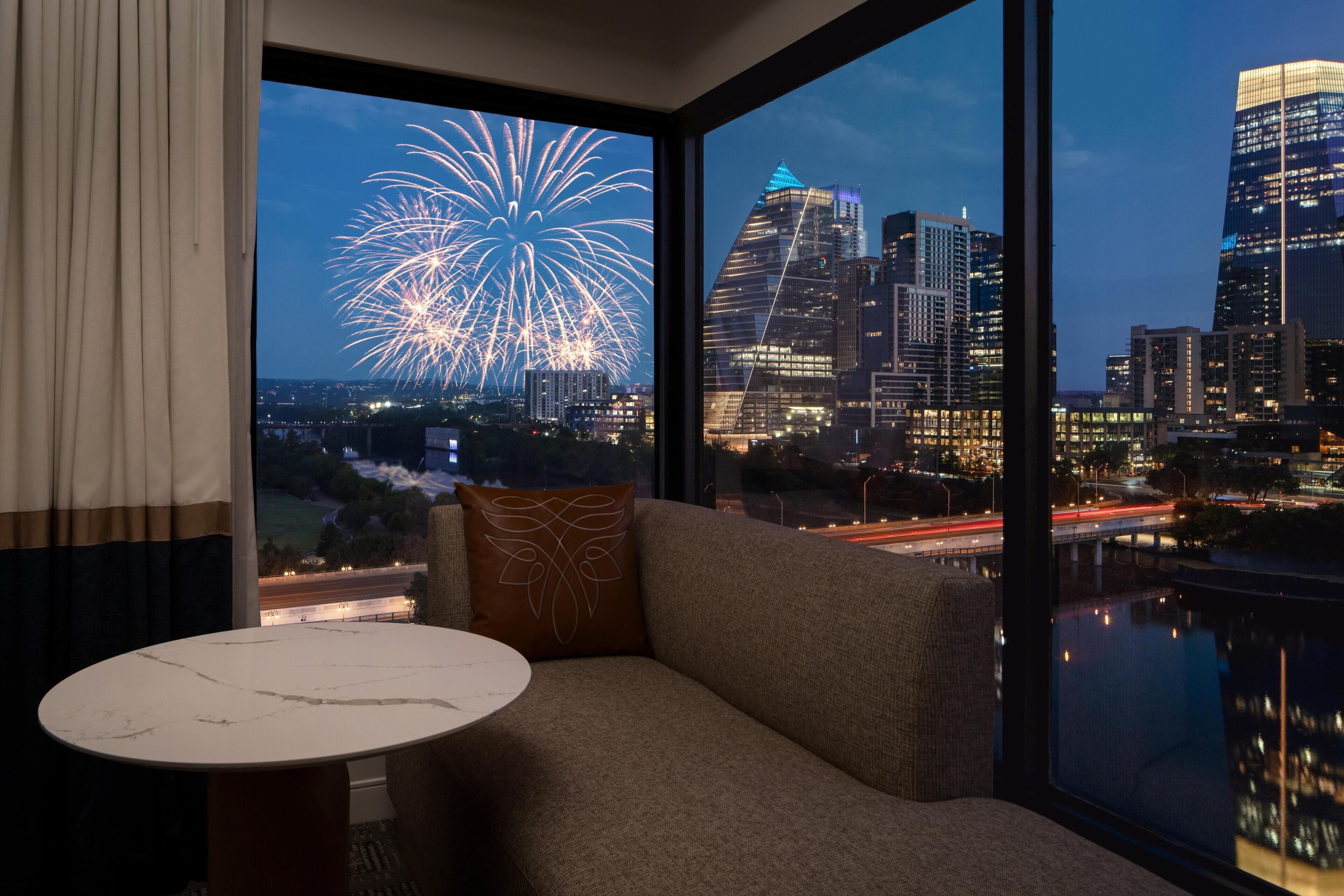 A room with a large window overlooking a city skyline and fireworks display.
