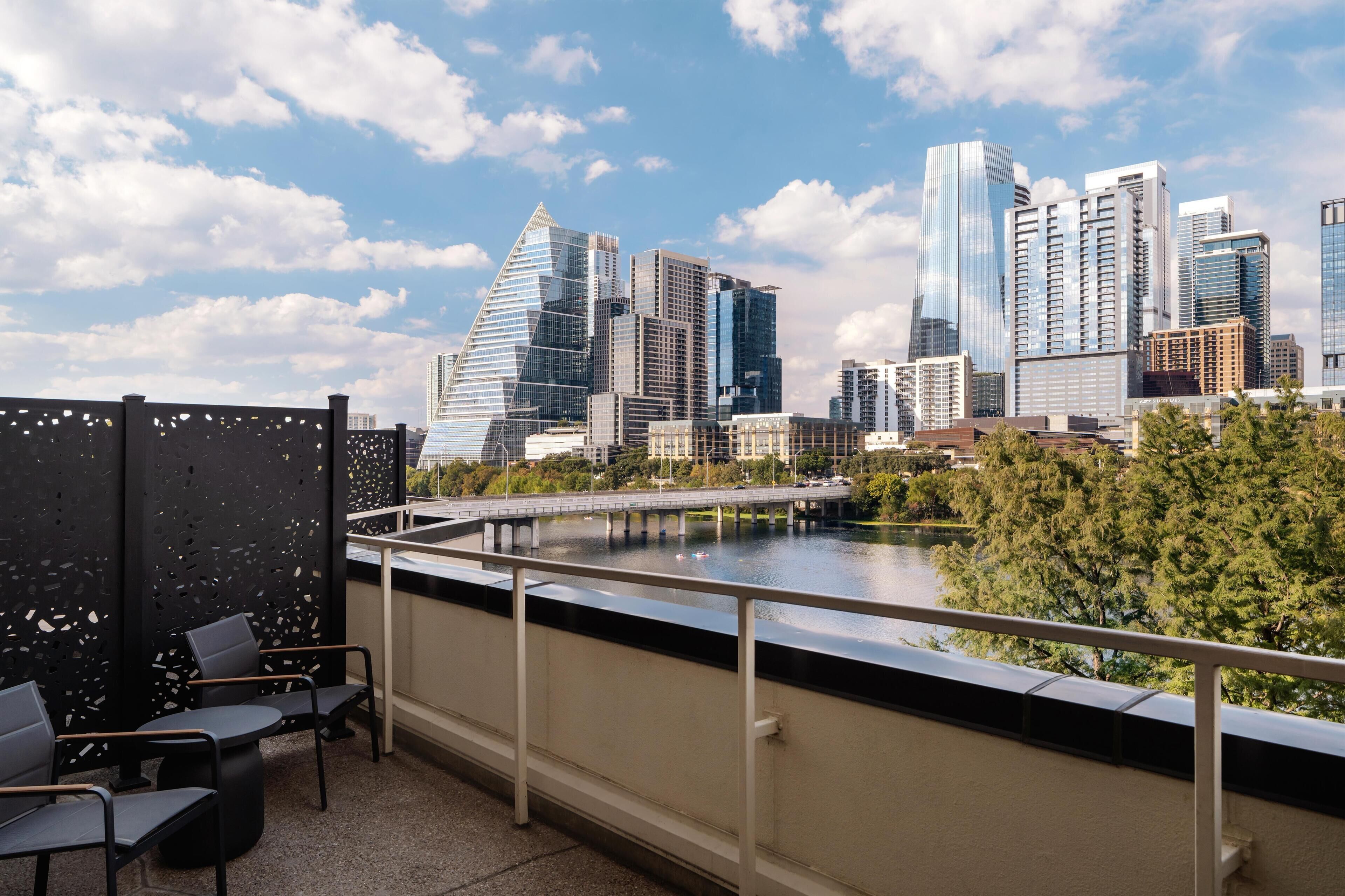 A city skyline with modern skyscrapers, a river, and a balcony with outdoor seating.