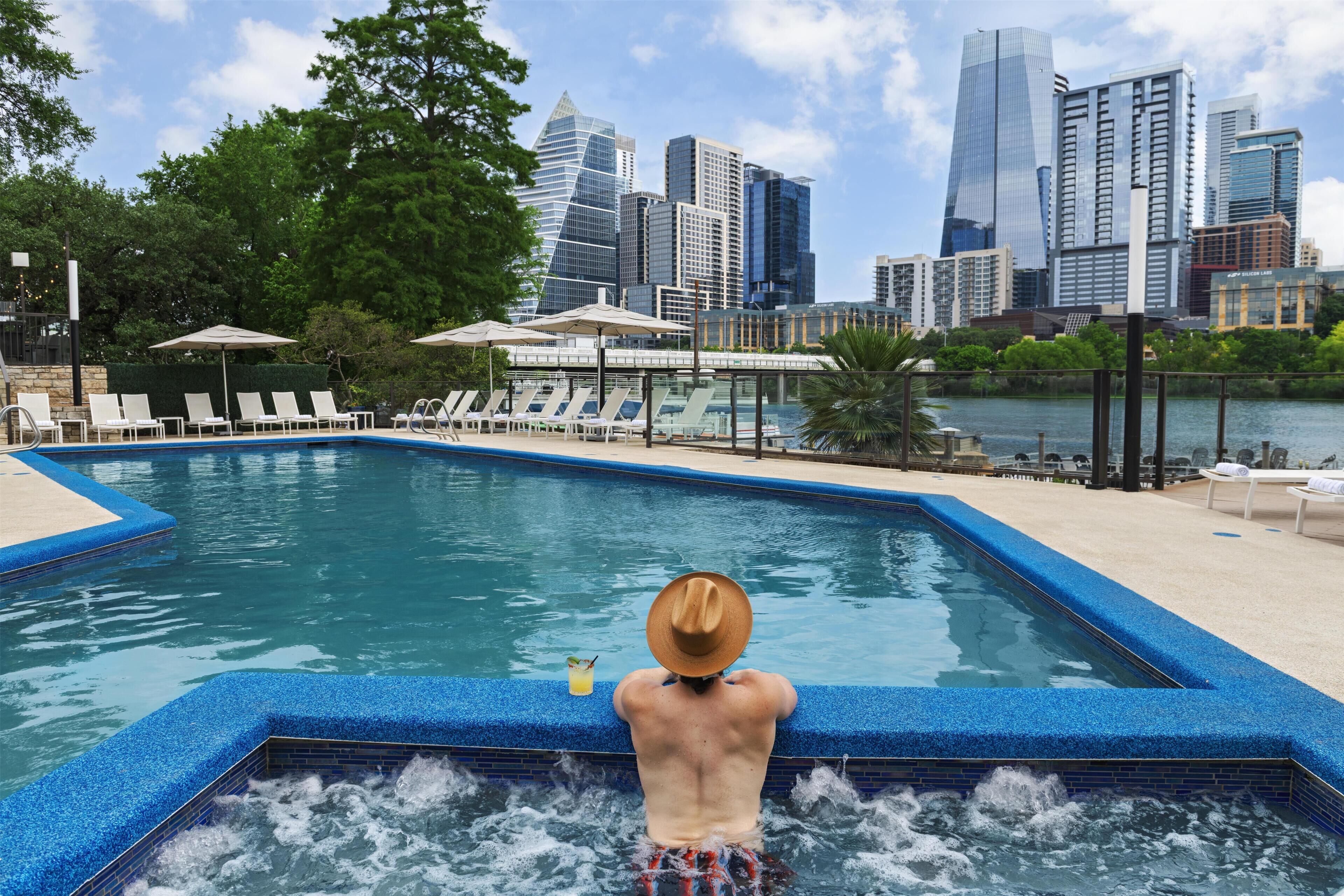 A pool with a city skyline in the background, lounge chairs, and umbrellas.
