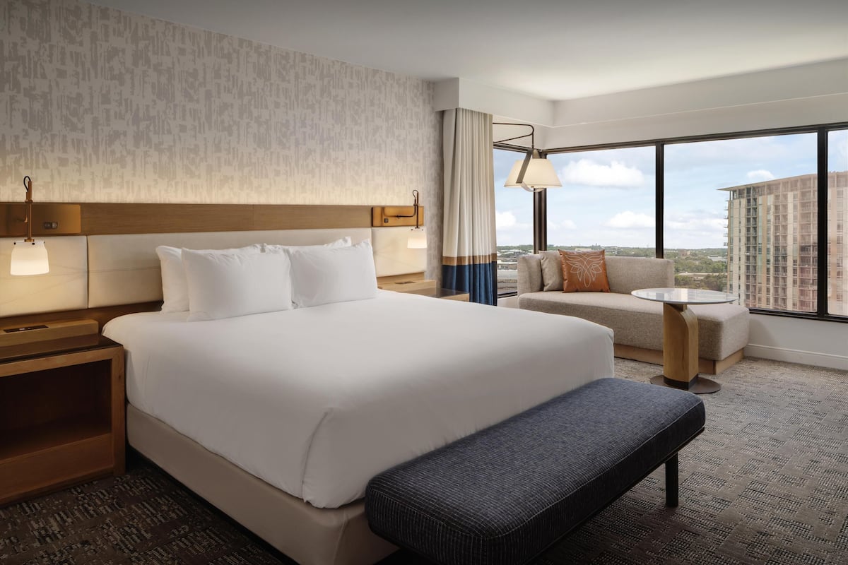 A hotel room with a large bed, a sofa, a small table, and a view of the city.