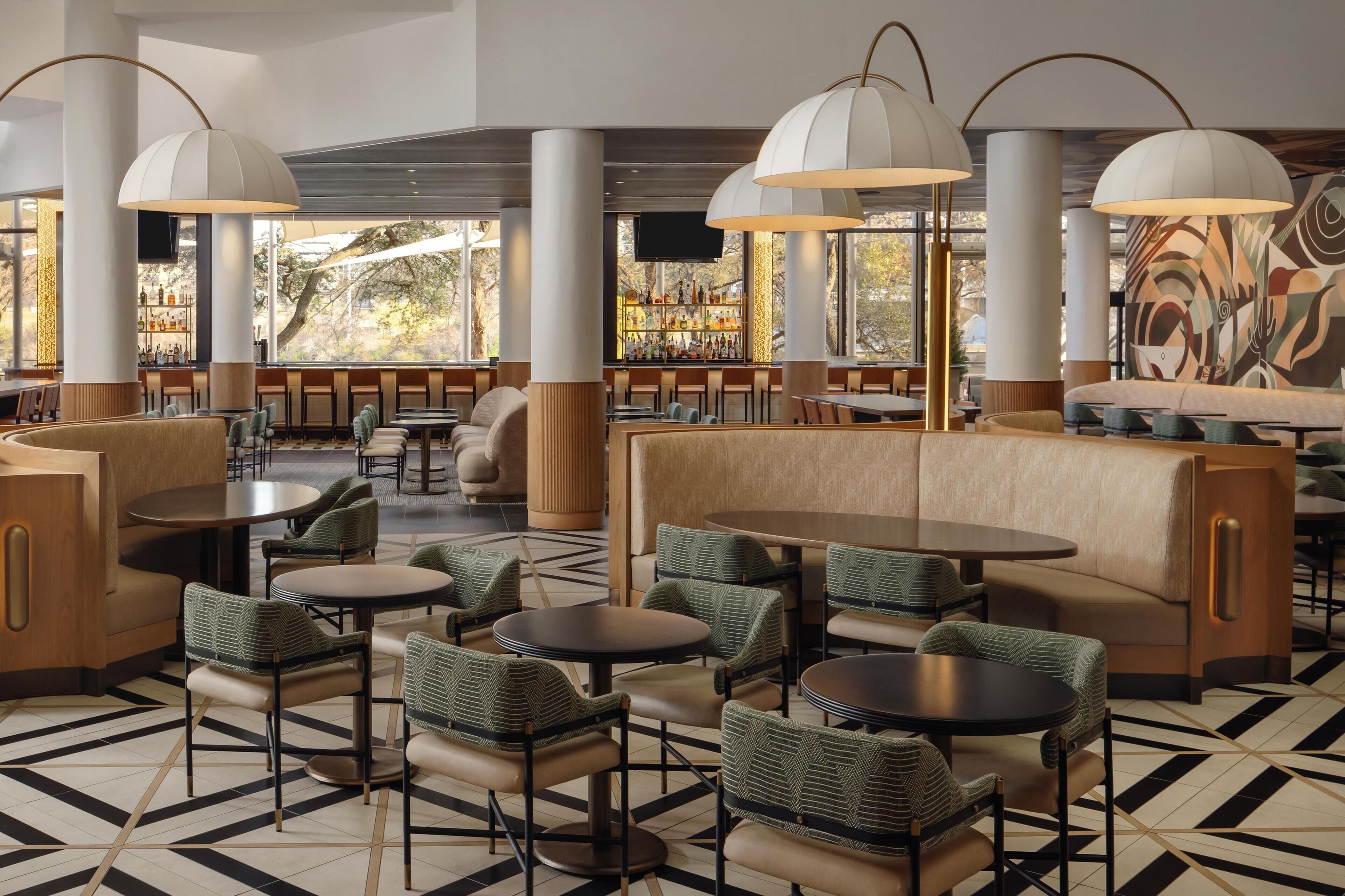 Un intérieur moderne avec des espaces aménagés pour s’asseoir, des tables et un bar où les bouteilles sont exposées.