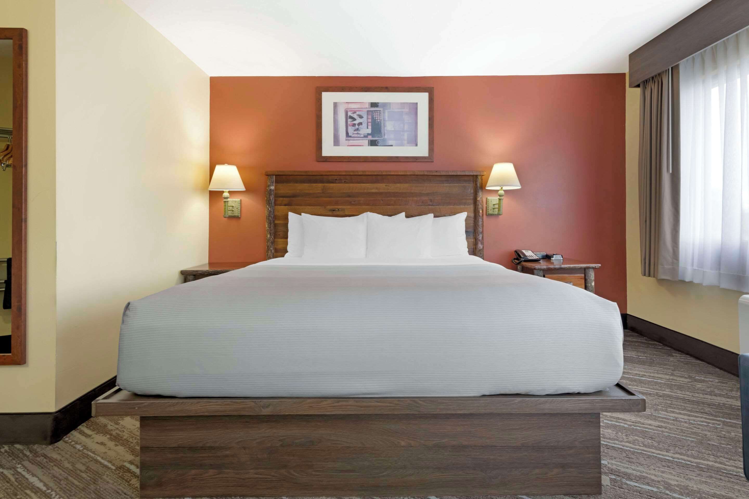 A hotel room with a large bed, two bedside lamps, a nightstand with a phone, and a framed picture on the wall.