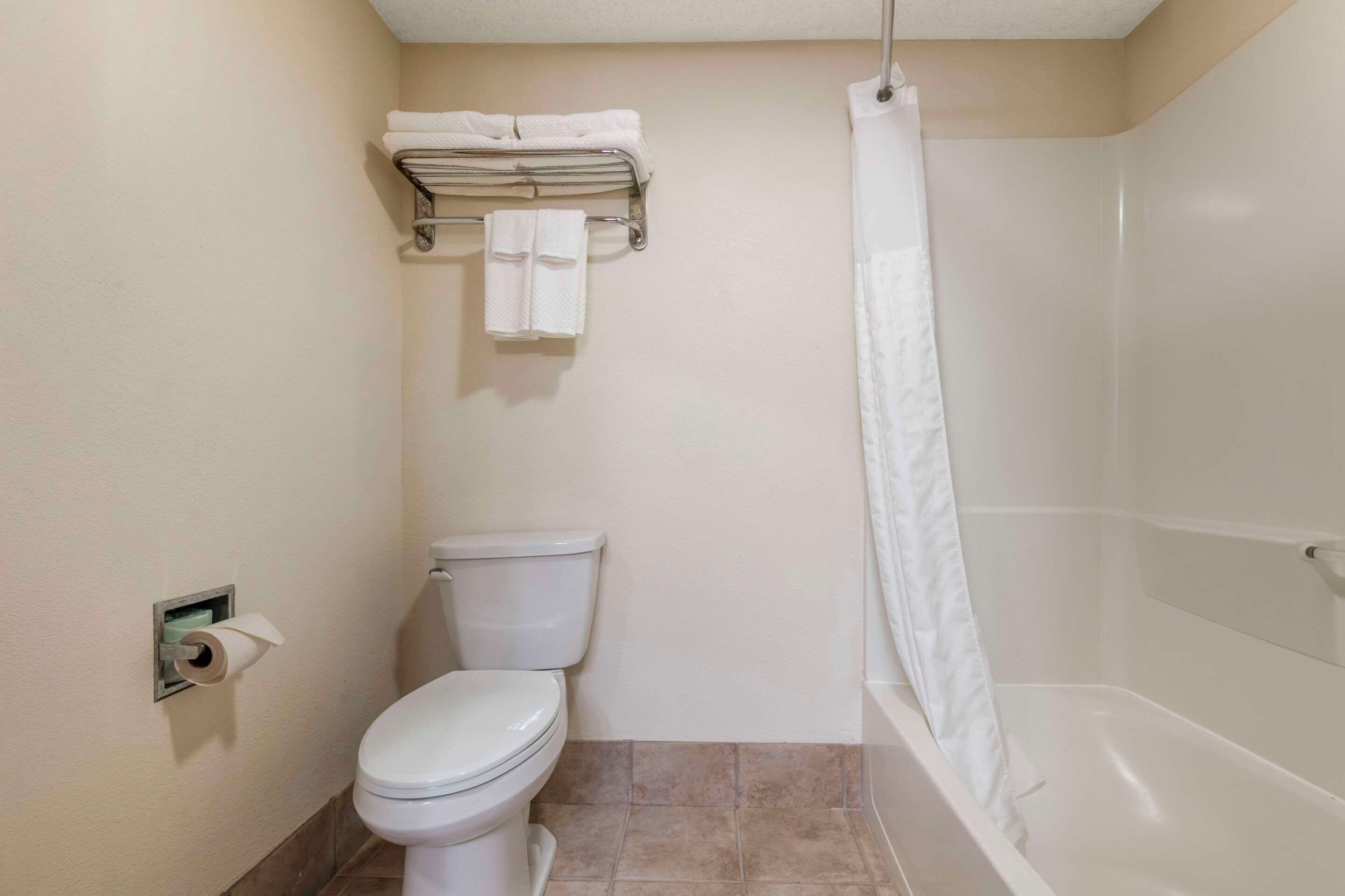 A bathroom with a toilet, a towel rack with towels, a shower curtain, and a toilet paper holder.