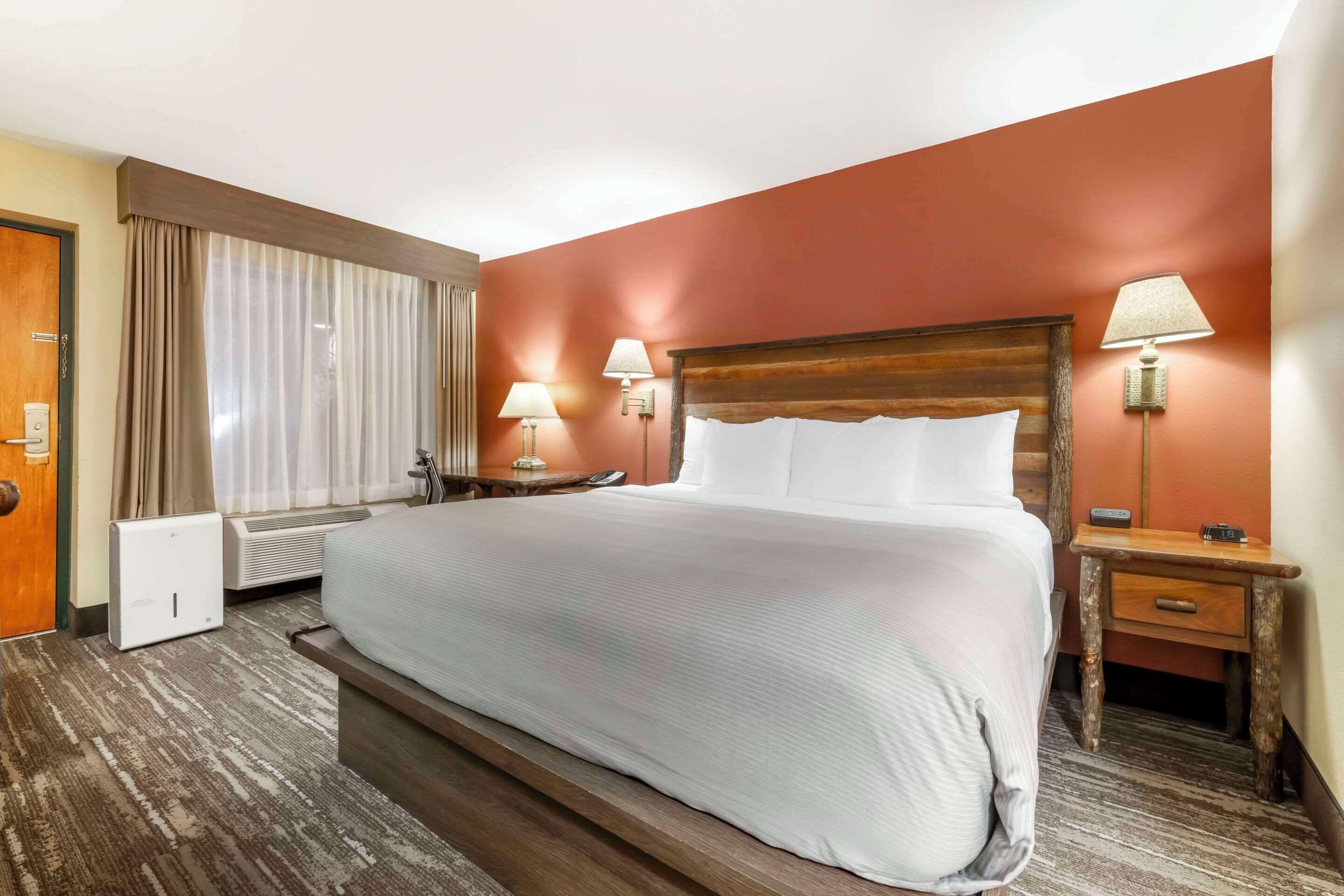 Habitación de hotel con una cama grande, dos lámparas de noche, una mesita de noche, un calentador y una ventana con cortinas.