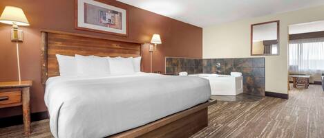 A hotel room with a large bed, a wooden headboard, two bedside lamps, a bathroom with a bathtub, a marble accent wall, and a small seating area with a table and chairs.