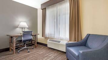 A hotel room with a desk, chair, and a blue sofa.