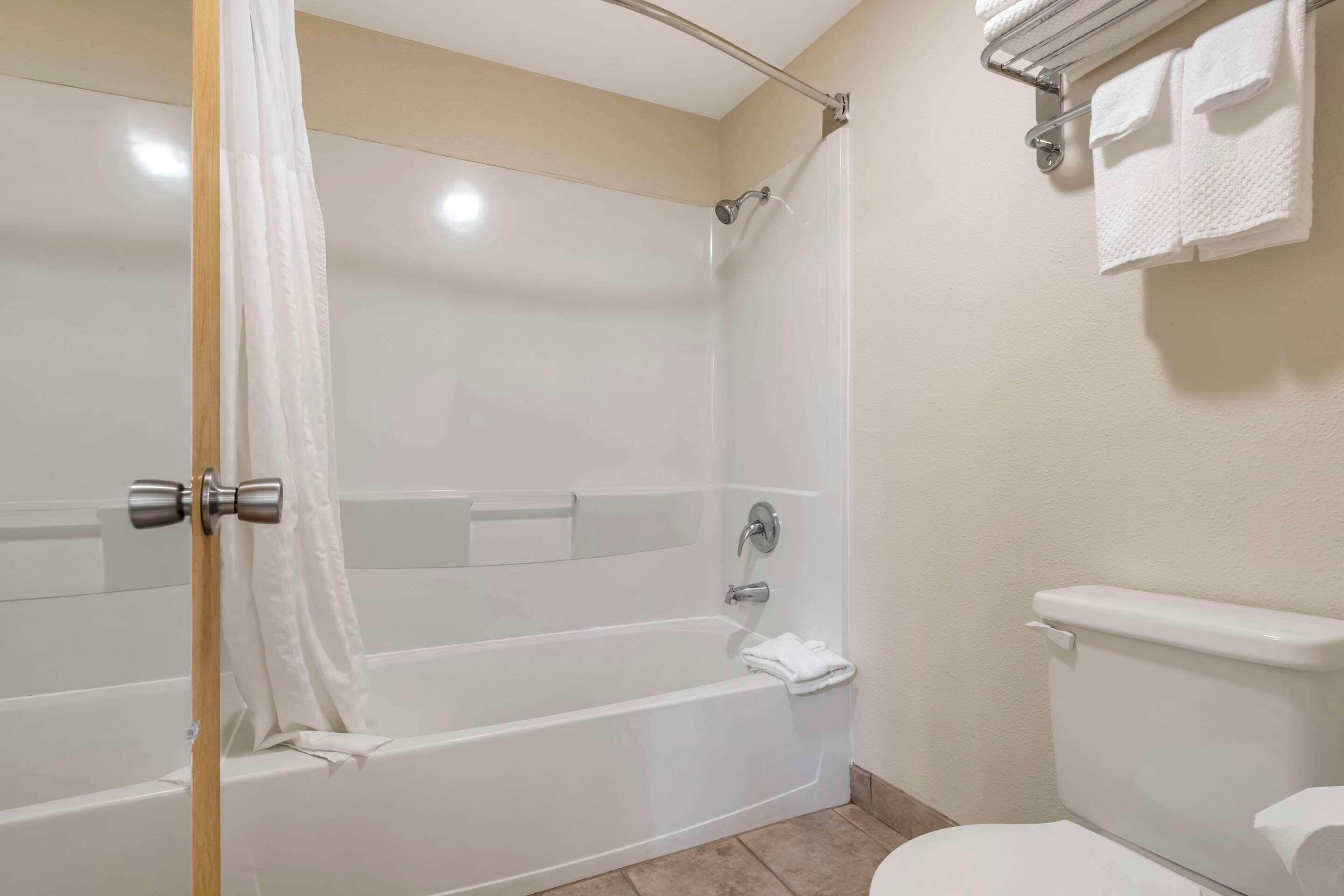 Et badeværelse med badekar, bruser, toilet og håndklædestang.