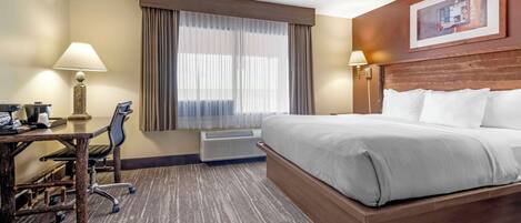 A hotel room with a large bed, a desk with a chair, a lamp, and a window with curtains.