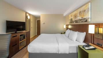 A hotel room with a bed, a TV, a desk with a lamp, and a painting on the wall.