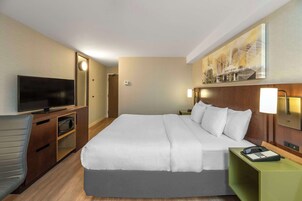 Una habitación de hotel con cama, televisión, escritorio con lámpara y un cuadro en la pared.
