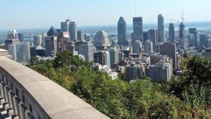 Une vue sur les toits d’une ville, avec des immeubles modernes de grande hauteur, un ciel dégagé et une étendue d’eau visible au loin.