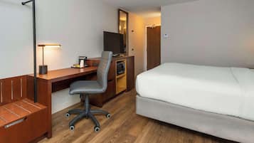 A hotel room with a bed, a desk with a chair, a TV, and a wooden bench.