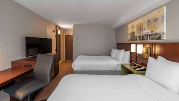 A hotel room with a desk, two beds, a TV, a painting, and a phone on the nightstand.