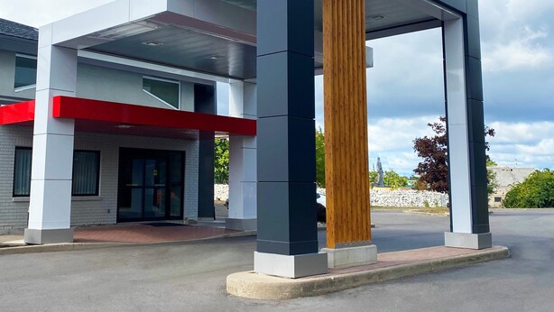 Un bâtiment moderne doté d’une colonne verticale en bois particulièrement visible, d’une touche de couleur rouge sur la façade et d’un ciel dégagé en arrière-plan.