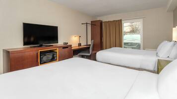 A hotel room with a flat-screen TV, a desk with a microwave, a chair, two beds, and a window with curtains.