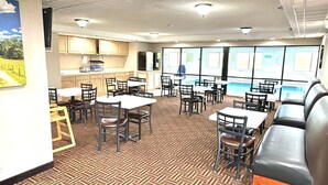 A restaurant with multiple tables and chairs, a kitchen area, and a view of a swimming pool. - Super 8 by Wyndham Chambersburg I-81 (Chambersburg)