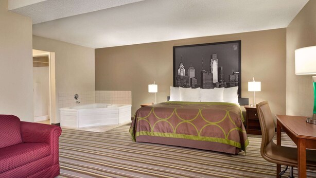 A hotel room with a bed, a red armchair, a desk, a chair, a bathtub, and a cityscape painting on the wall. - Super 8 by Wyndham Chambersburg I-81 (Chambersburg)