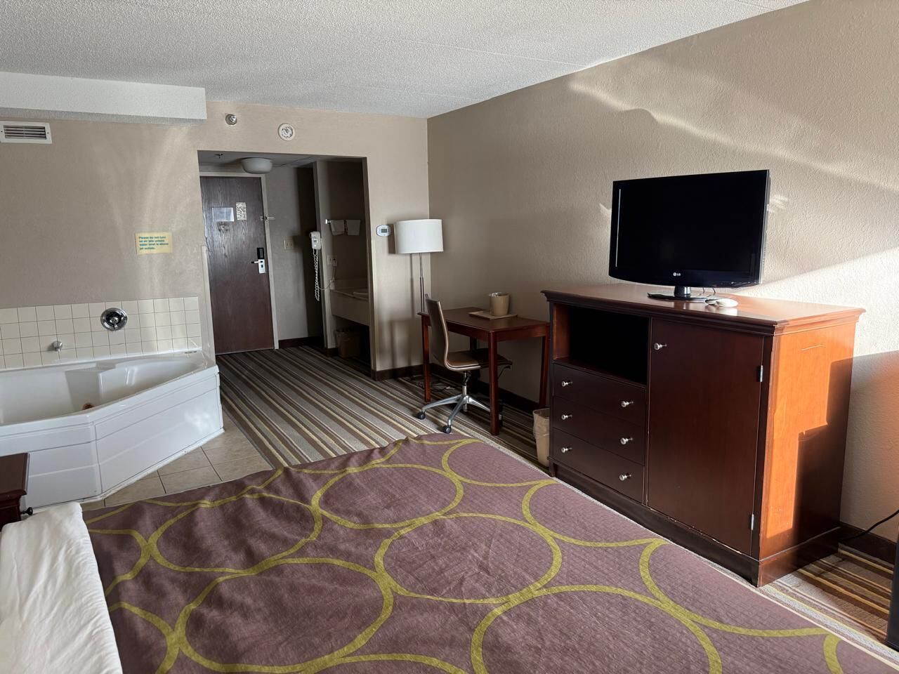 Habitación de hotel con cama, escritorio, televisor, cómoda y baño con bañera e inodoro.