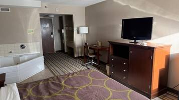 Habitación de hotel con cama, escritorio, televisor, cómoda y baño con bañera e inodoro.