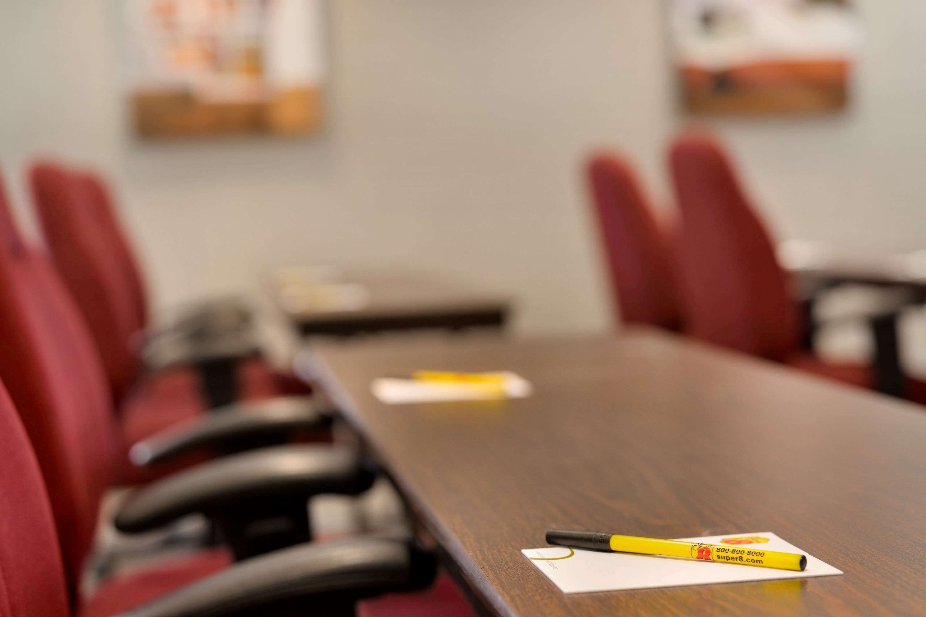 Un salón de conferencias con una larga mesa, sillas rojas y un marcador amarillo sobre la mesa.
