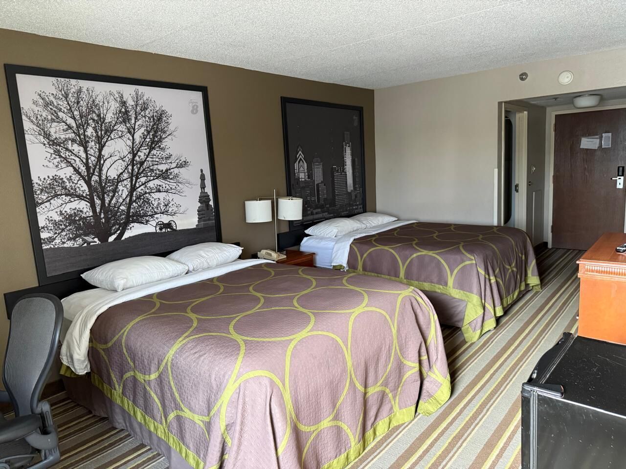 A hotel room with two beds, a desk, a chair, and a dresser.