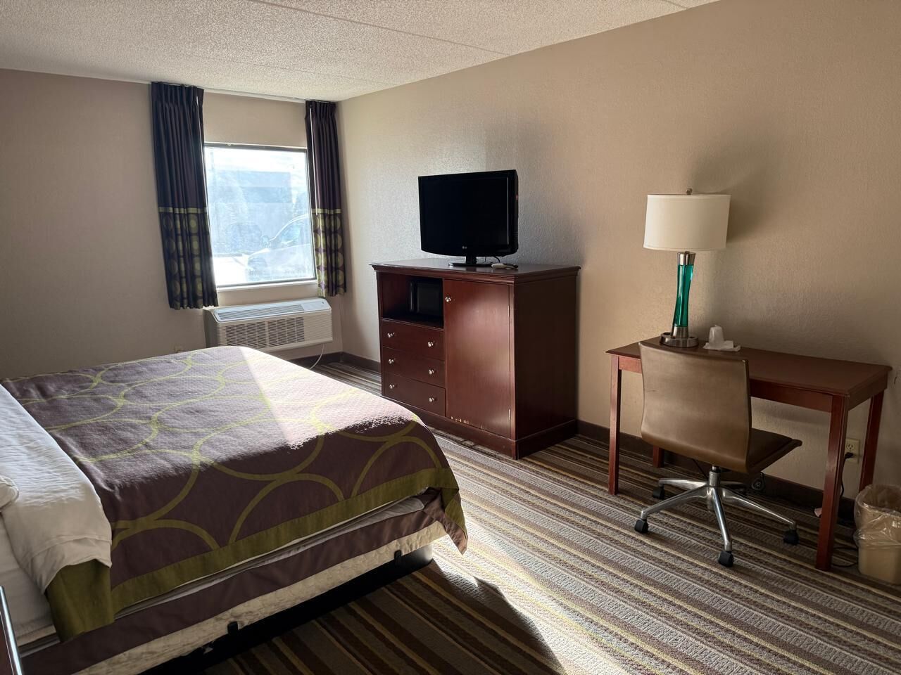 A hotel room with a bed, a desk, a chair, a television, and a lamp.