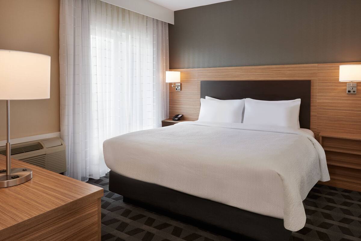 A hotel room with a large bed, a bedside table with a lamp, a phone, and a wall-mounted light.
