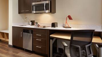 A modern kitchen with a built-in microwave, dishwasher, and a wooden dining table with a chair.