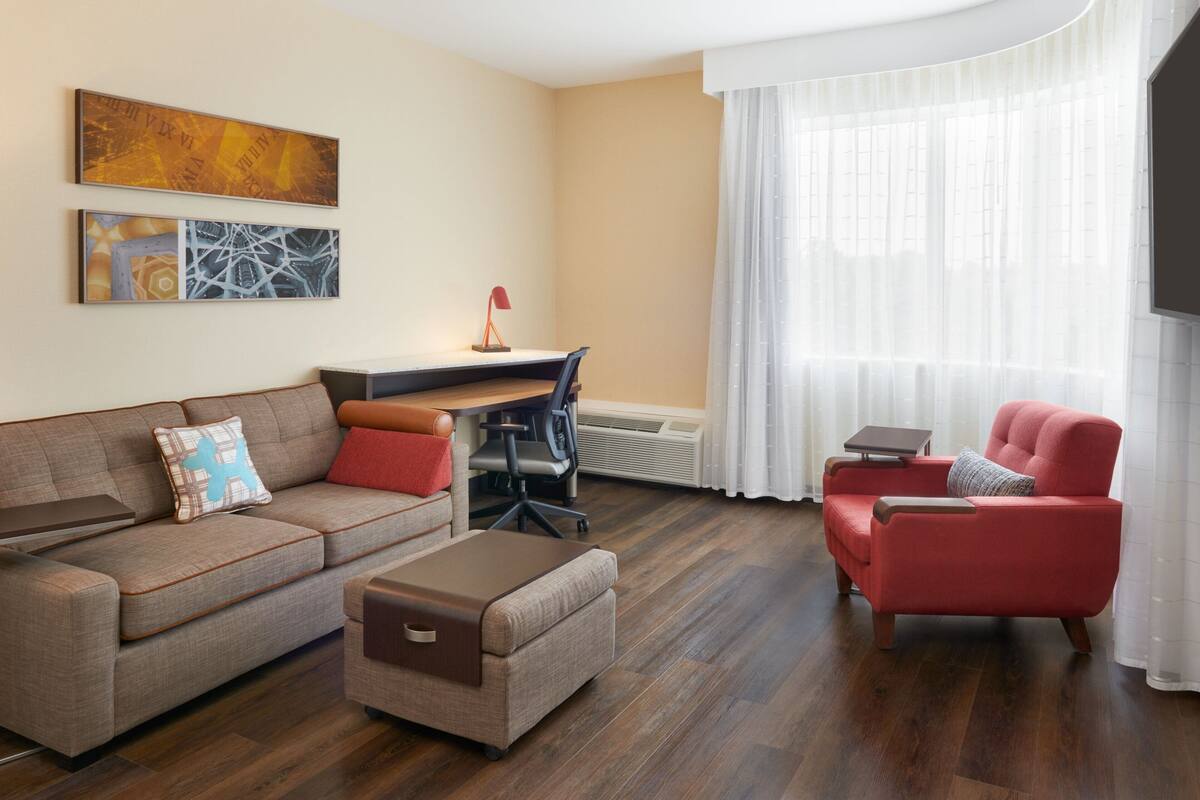 A modern living room with a sofa, armchair, ottoman, and a desk with a chair.