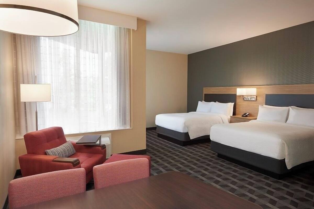 A hotel room with two beds, a sofa, a table, and a lamp.