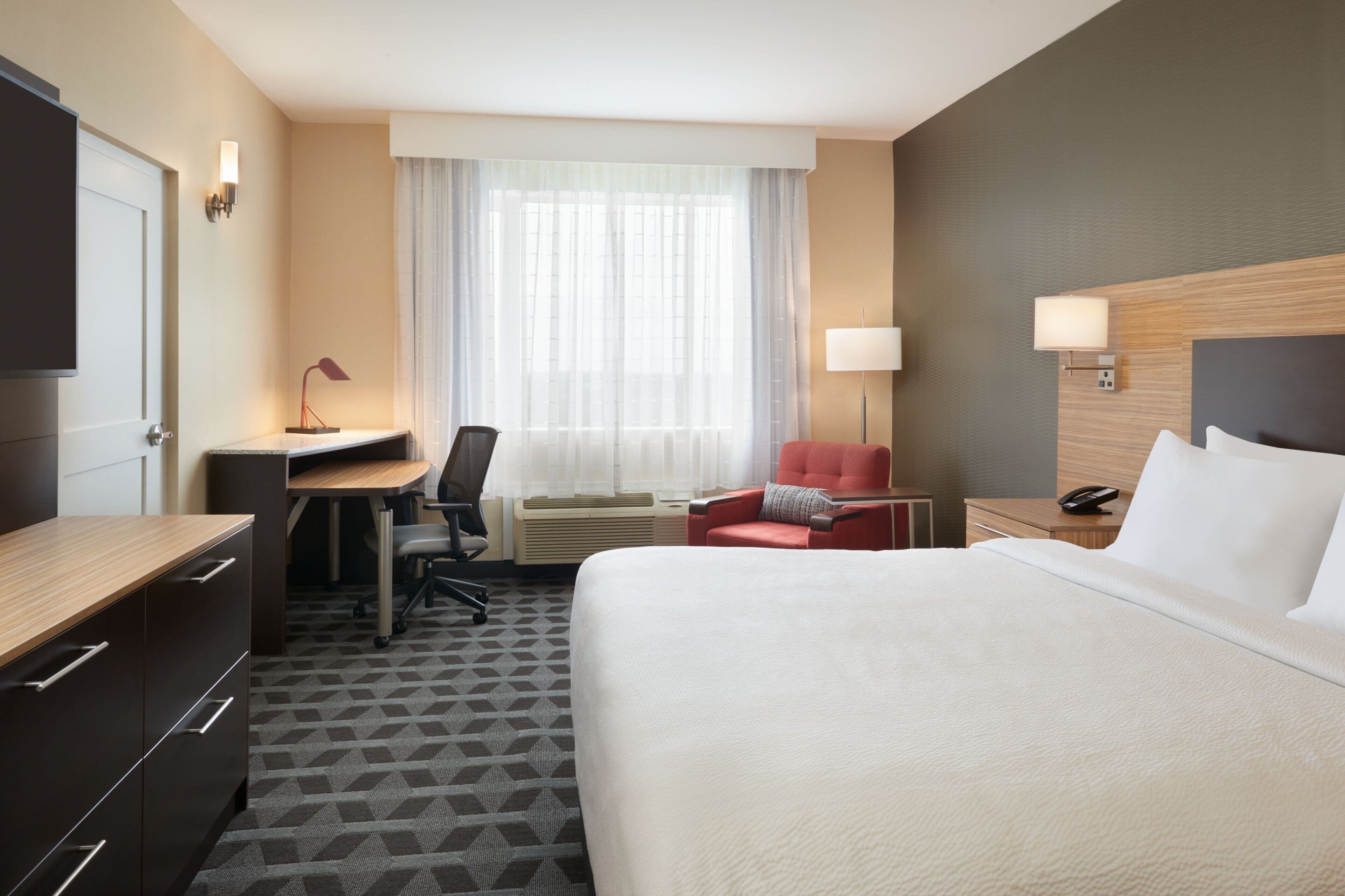 Une chambre d’hôtel avec un lit, un bureau, une chaise et une fenêtre avec des rideaux.