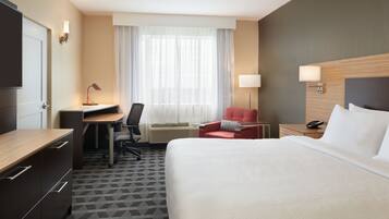 A hotel room with a bed, desk, chair, and a window with curtains.
