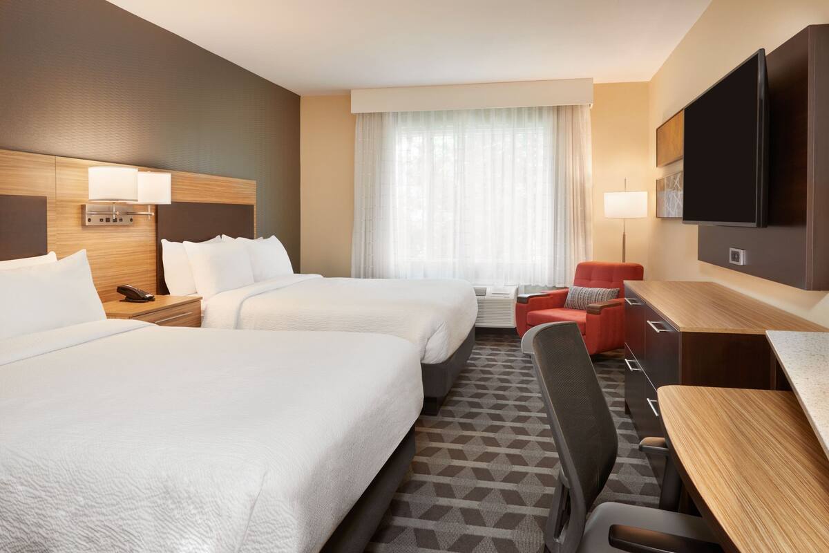A hotel room with two beds, a desk, a chair, a TV, and a window with curtains.