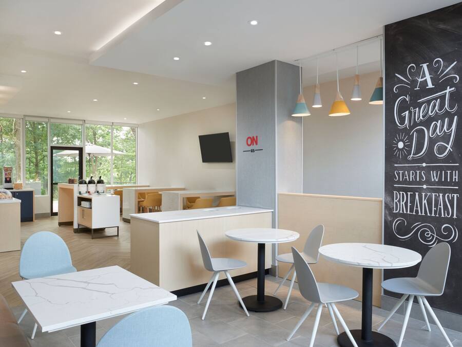A modern cafe with round tables and chairs, a counter with a 'ON' sign, and a 'A Great Day Starts with Breakfast' sign.