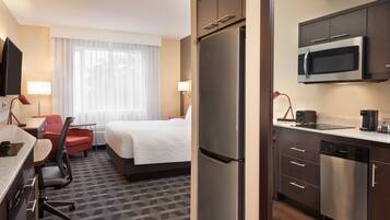 Habitación de hotel con cama, escritorio, silla y kitchenette que incluye refrigerador, microondas y cafetera.