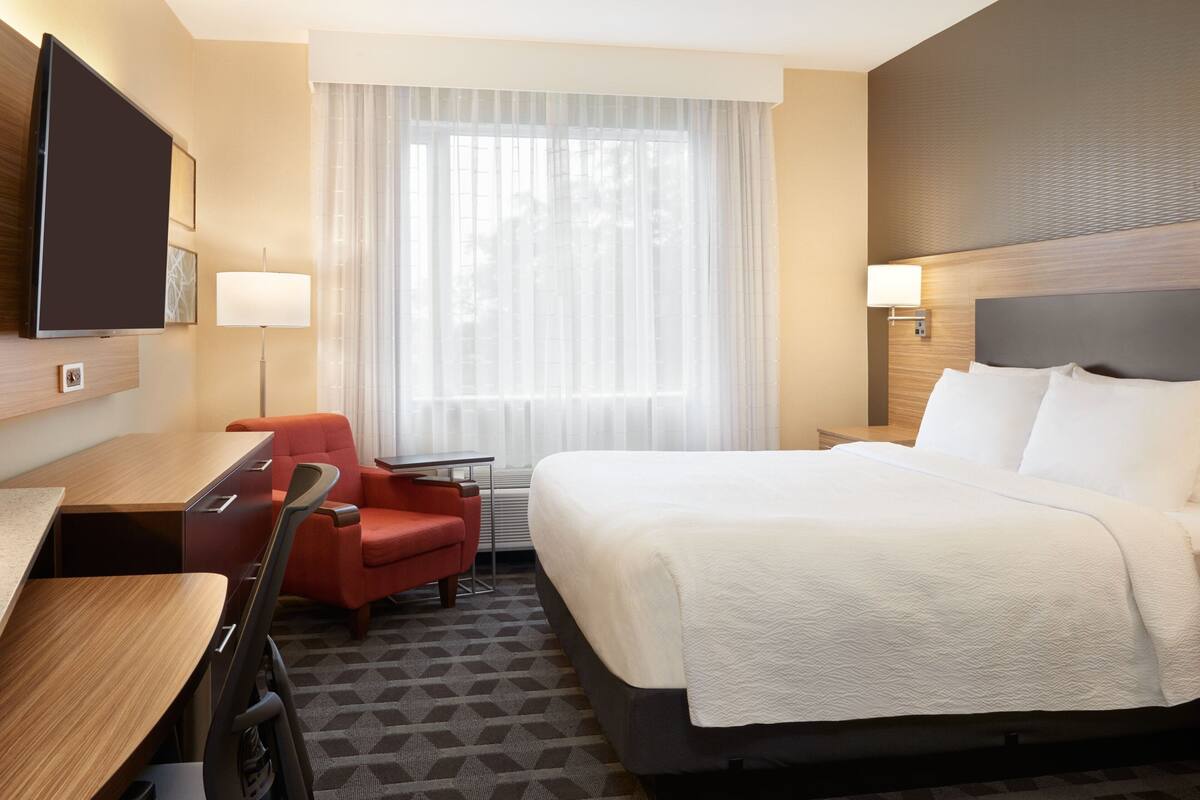 A hotel room with a bed, a desk, a chair, a TV, and a window with curtains.