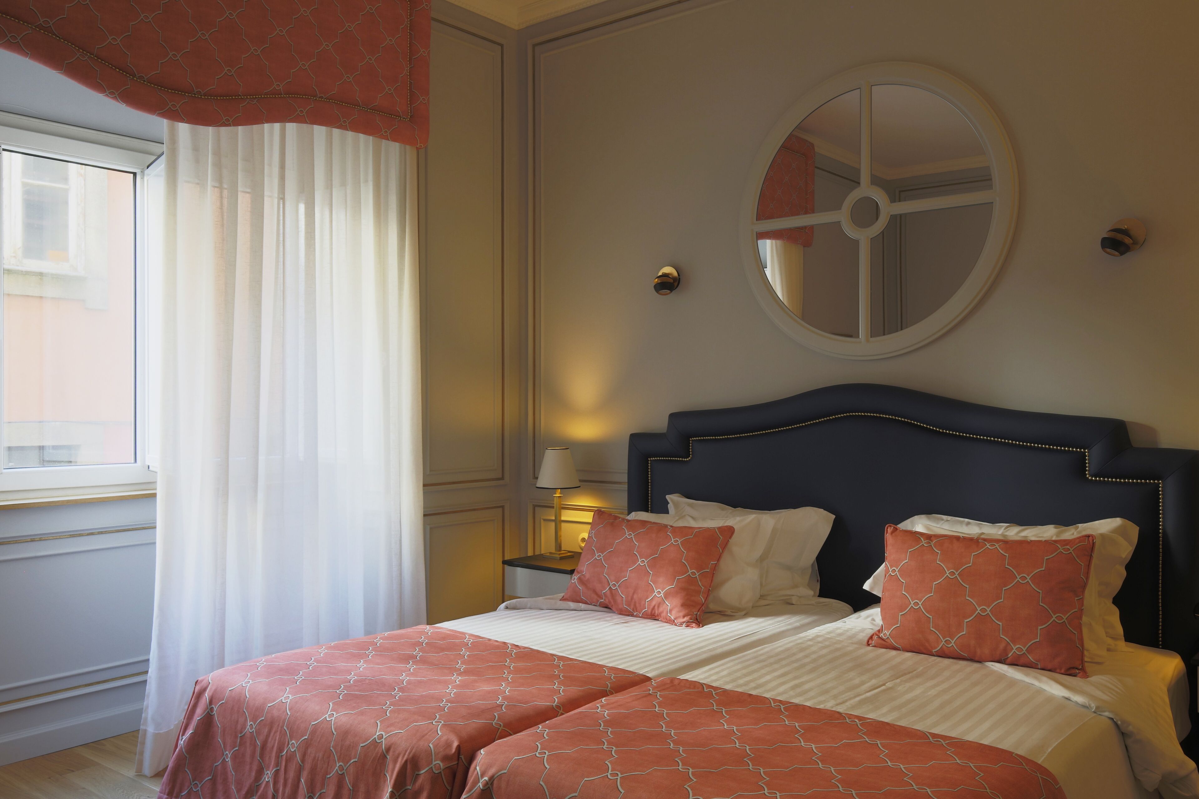 A double bed with a dark headboard, two matching pillows, and a window with sheer curtains.