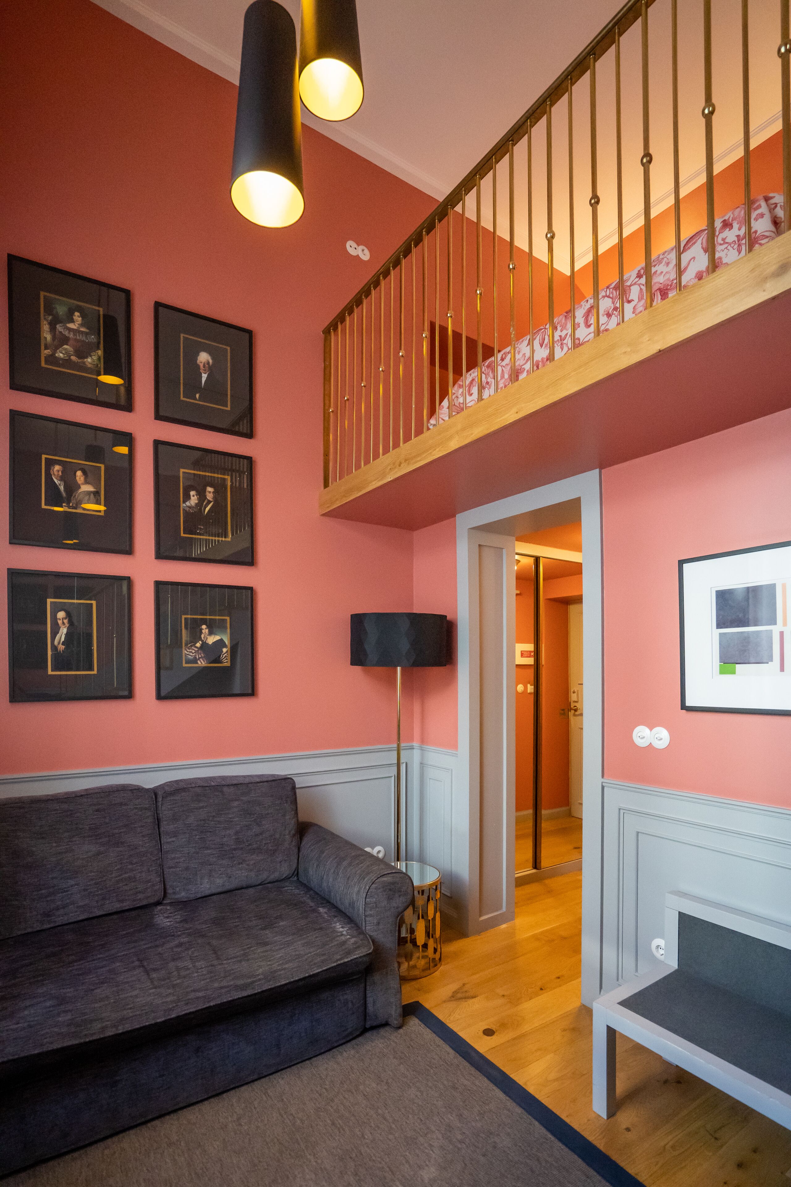 A modern living room with a grey sofa, a wooden staircase, and framed pictures on the walls.