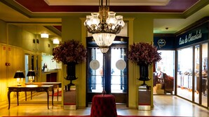A lobby with a chandelier, a red ottoman, a table with lamps, and a shop named "Casa do Chocolate". - Grande Hotel do Porto (Porto)