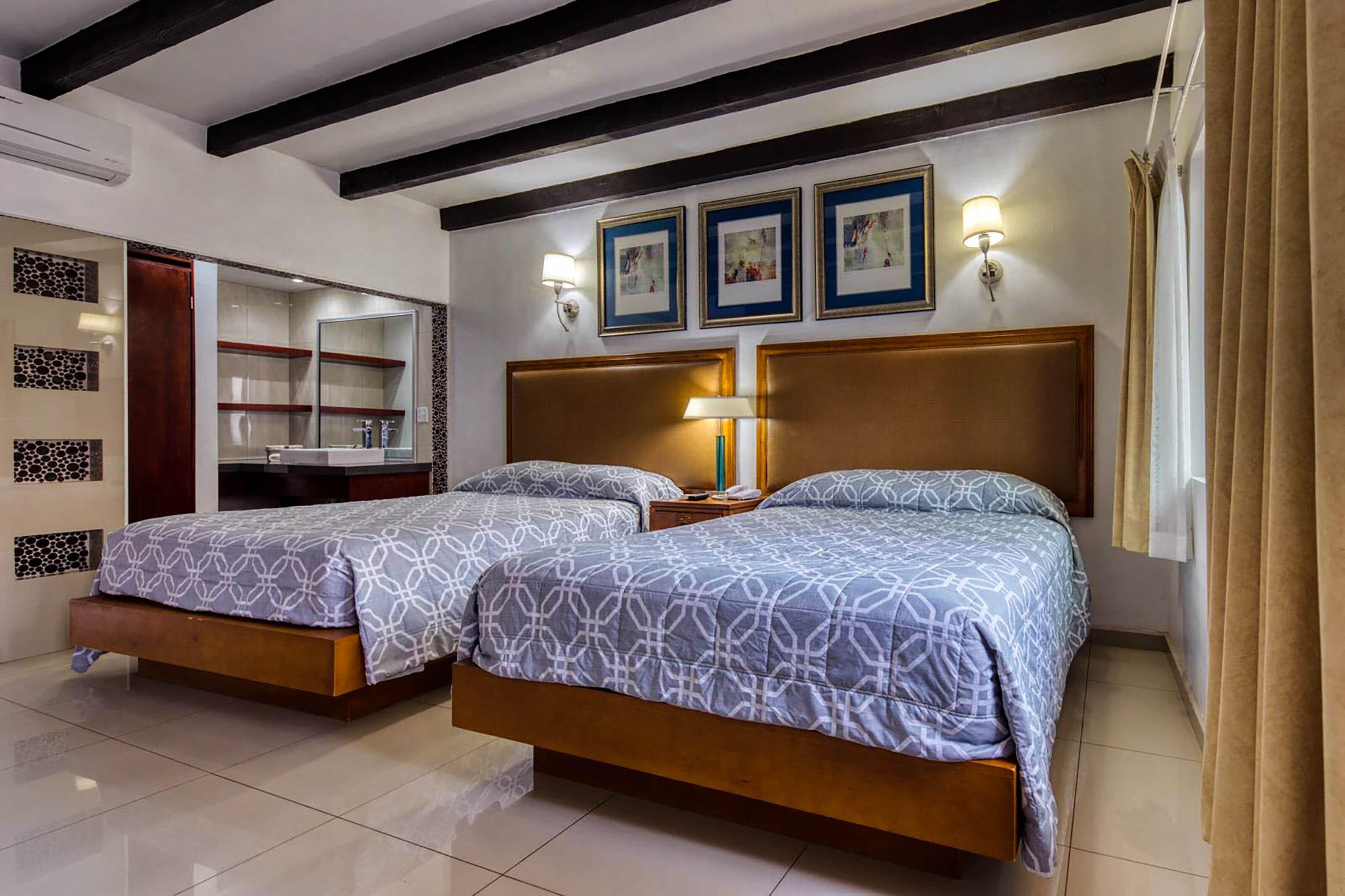 A room with two beds, a wardrobe, a mirror, and framed pictures on the wall.